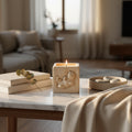 A square cream-colored candle holder made of textured concrete or stone, featuring a relief carving of a French bulldog lying down. A lit candle is placed inside, casting a warm glow against a neutral gray background.