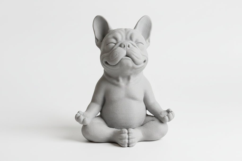 Gray ceramic bulldog figurine sitting in a meditative pose on a light gray background