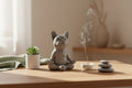 Gray ceramic bulldog figurine sitting in a meditative pose on a light gray background